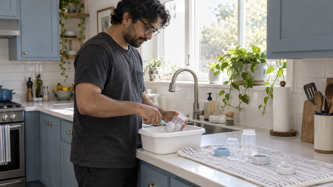 A father washing a baby bottle in a dedicated basin beside separated bottle parts drying on a clean towel.