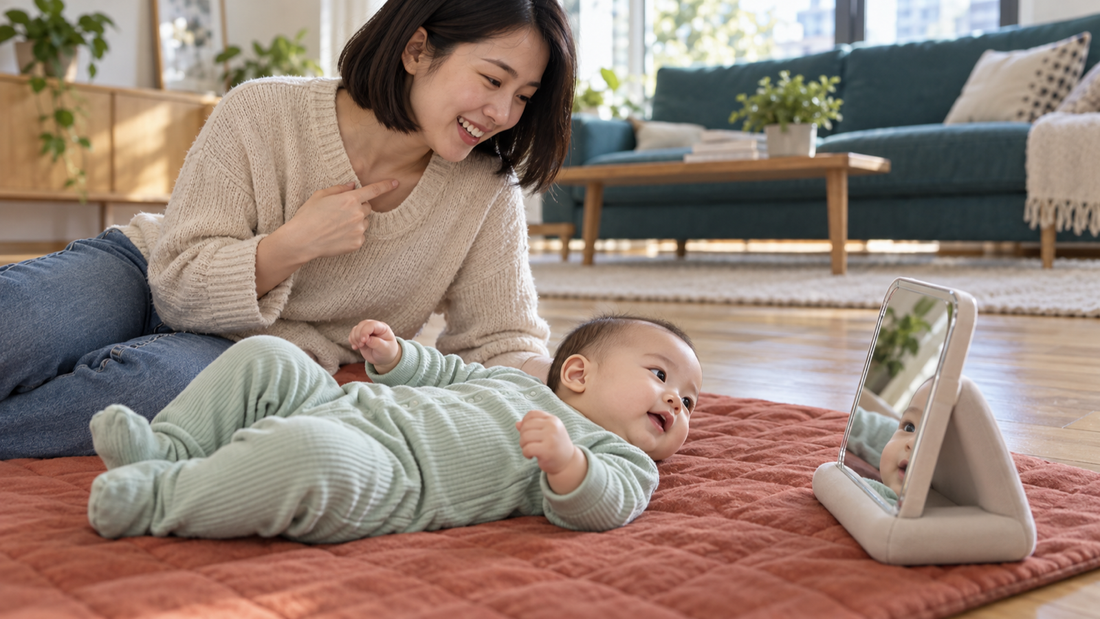 A mother and her awake baby playing beside a small supported baby mirror on a rust-colored floor mat.