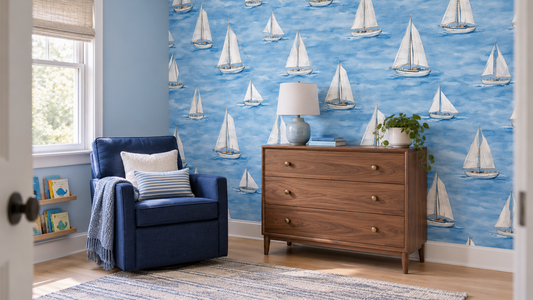 A blue nursery sitting corner with sailboat wallpaper, a navy chair and a walnut dresser.