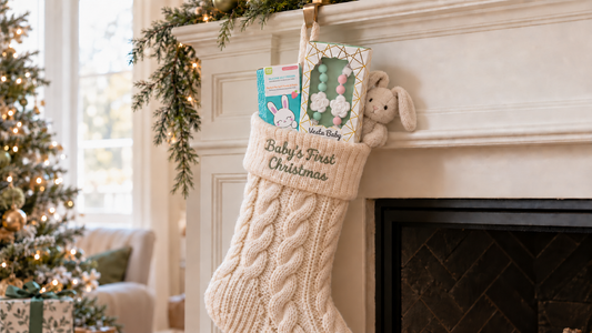 An ivory Baby's First Christmas stocking on a fireplace mantel, with boxed baby gifts and a beige plush bunny.