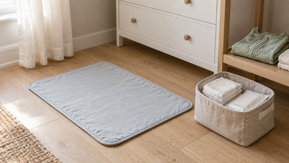 A light gray changing mat beside a linen caddy of diapers and wipes, with spare baby clothes on an oak shelf.