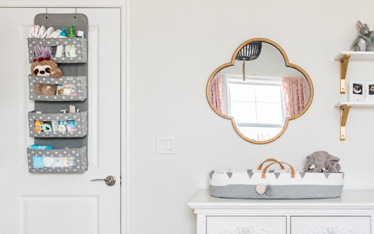 Gray star-pattern hanging organizer and gray-and-white changing basket beside a gold mirror in a bright nursery.