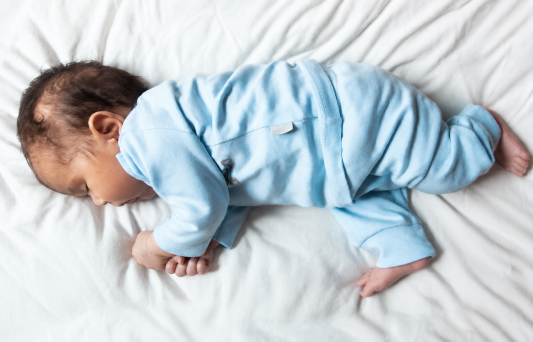 Baby wearing pale blue clothes lying on a white sheet.